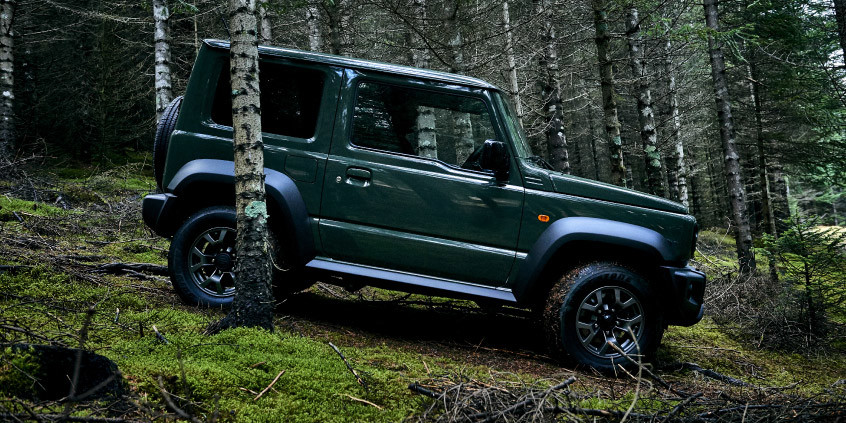 Imagen de un Jimny color verde jungla andando en un bosque.