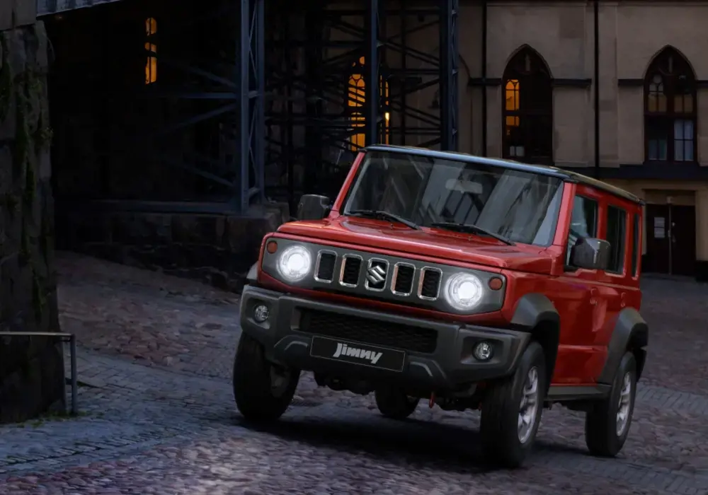 SUV Suzuki Jimny de color rojo brillante se conduce cuesta arriba por una calle empedrada