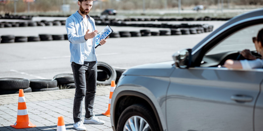 Persona realizando prácticas de manejo en un estacionamiento, mientras lo evalúan.